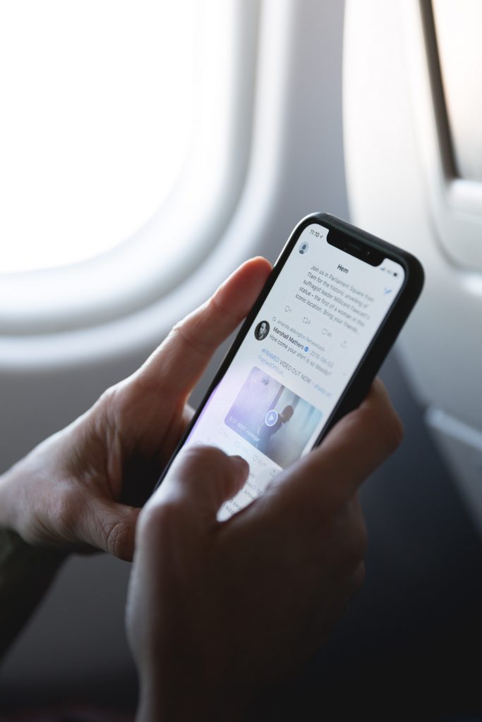 A person's hands holding a mobile phone. The phone is displaying Twitter and the person's thumb is touching the screen.