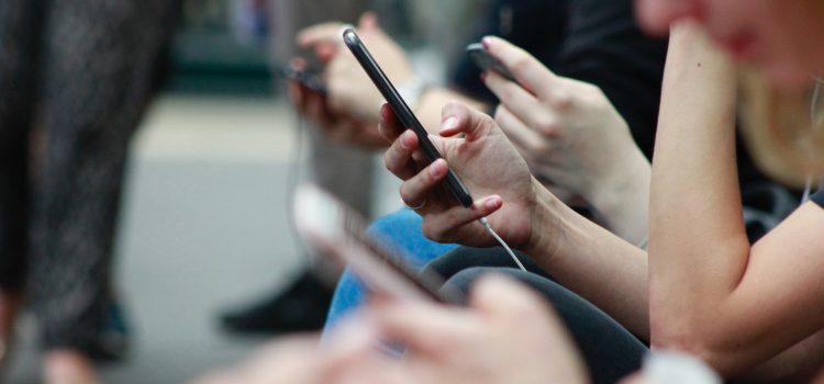 People holding smartphones in their hands. The focus of the image is on the hands holding the smartphones. Only one person's face appears and it is blurred.