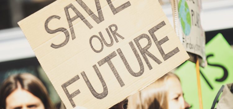 Young adult holding a "SAVE OUR FUTURE" sign. Other people appear behind the young adult, one of whom is also holding a sign with a picture of the globe.