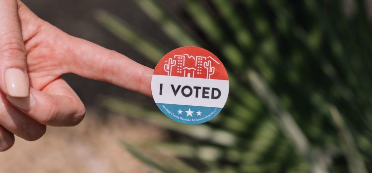 Finger holding a "I VOTED" sticker